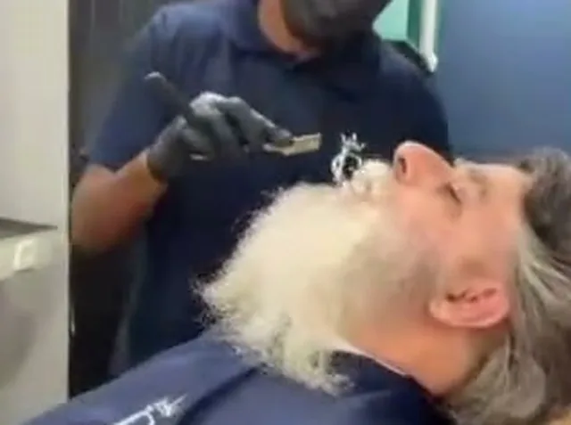 Barbeiro de luvas alinhando a barba de um cliente na navalha